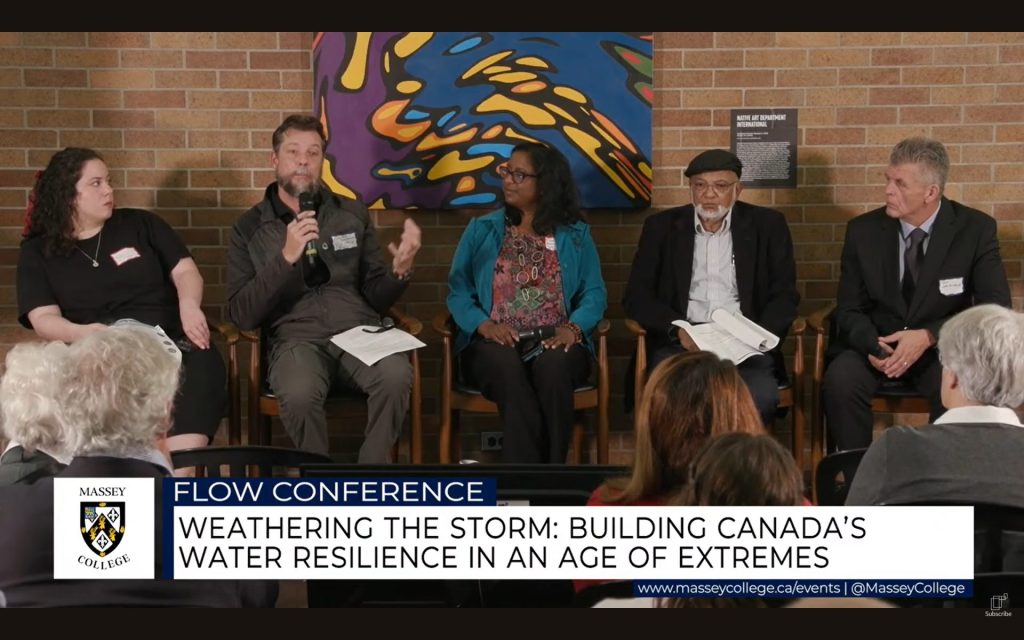 Photo of the five panellists on the first panel at the FLOW Conference. They sit side-by-side in chairs. POLIS' Oliver M. Brandes is holding a microphone and speaking. He is sitting second from left.